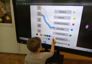 Chłopiec pracuje przy monitorze interaktywnym - wykonuje kartę pracy - dni tygodnia, wybiera na paletce kolor.